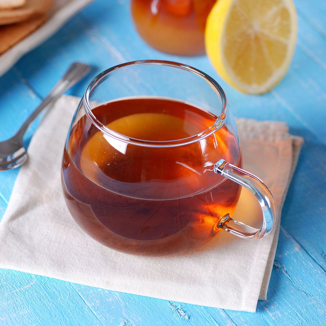 Warm Bread Pudding Tea in clear mug on tan napkin on blue table next to lemon slice and spoon
