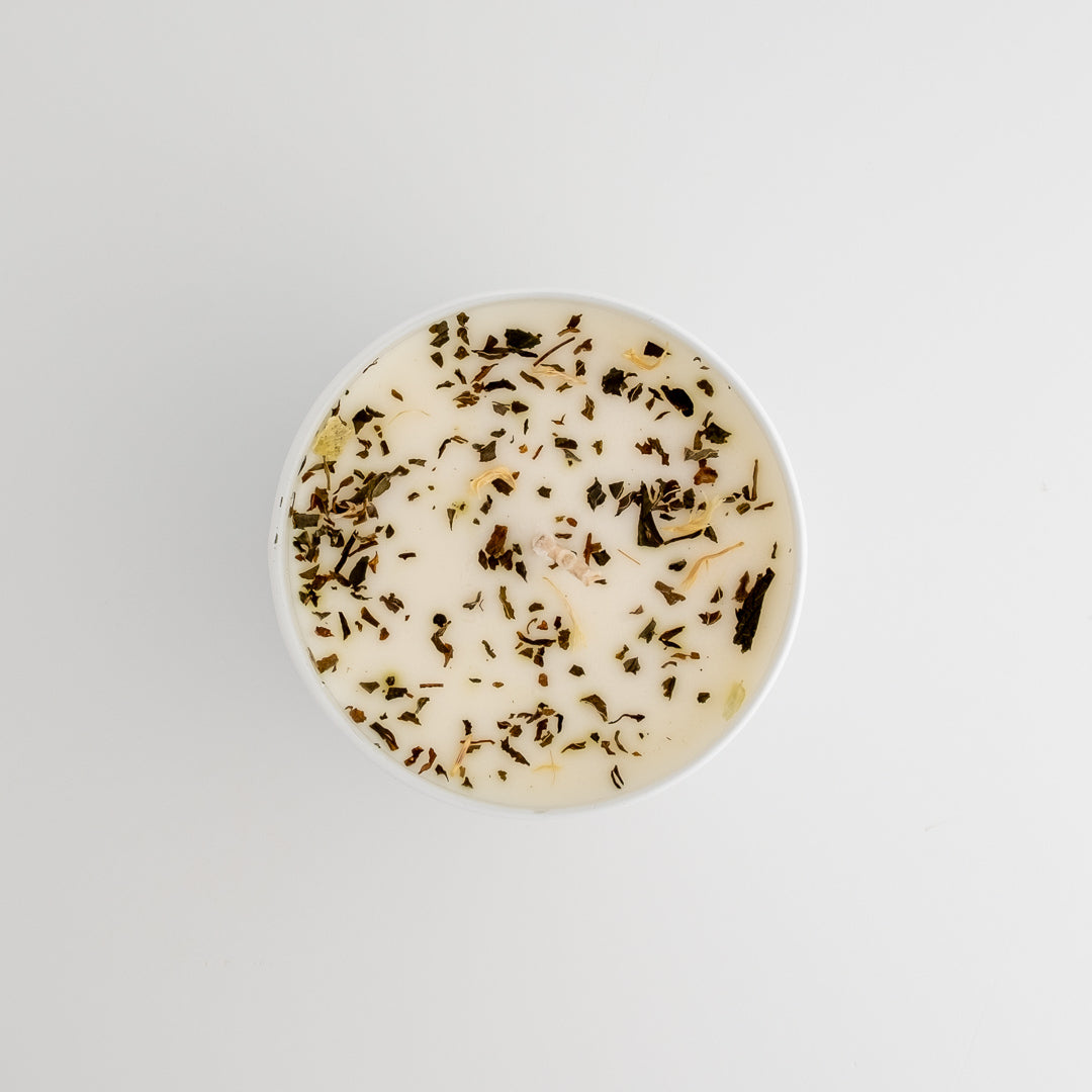 Round candle with visible herbs on a light gray background
