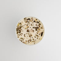 Round candle with visible herbs on a light gray background
