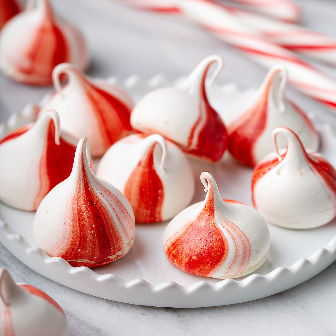 Red and white striped meringues on a white plate with candy canes in the background.